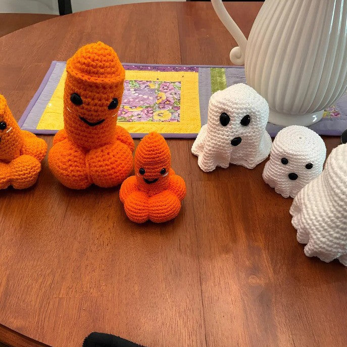 Funny handmade-style crochet Halloween ghost and naughty pumpkin decorations in different sizes displayed on a wooden table.