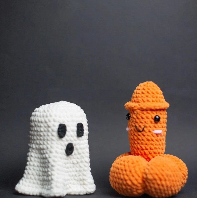 White crochet Halloween ghost beside a cheeky orange pumpkin-shaped novelty figure with a smiling face, photographed against a dark background.